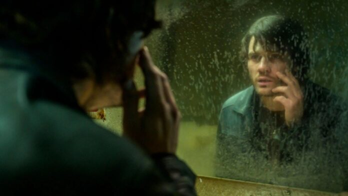 return-to-silent-hill-trailer-pyramid-head Primer plano de Jeremy Irvine (James Sunderland) mirando su reflejo en un espejo sucio y empañado en la película Return to Silent Hill.