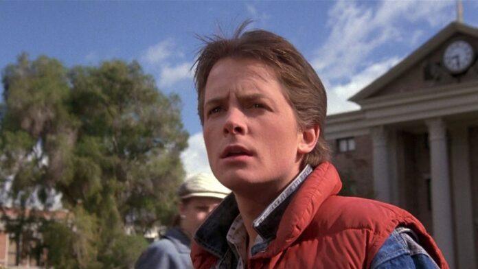 Michael J. Fox como Marty McFly en la película Regreso al Futuro (1985), sonriendo con su característico chaleco vaquero.